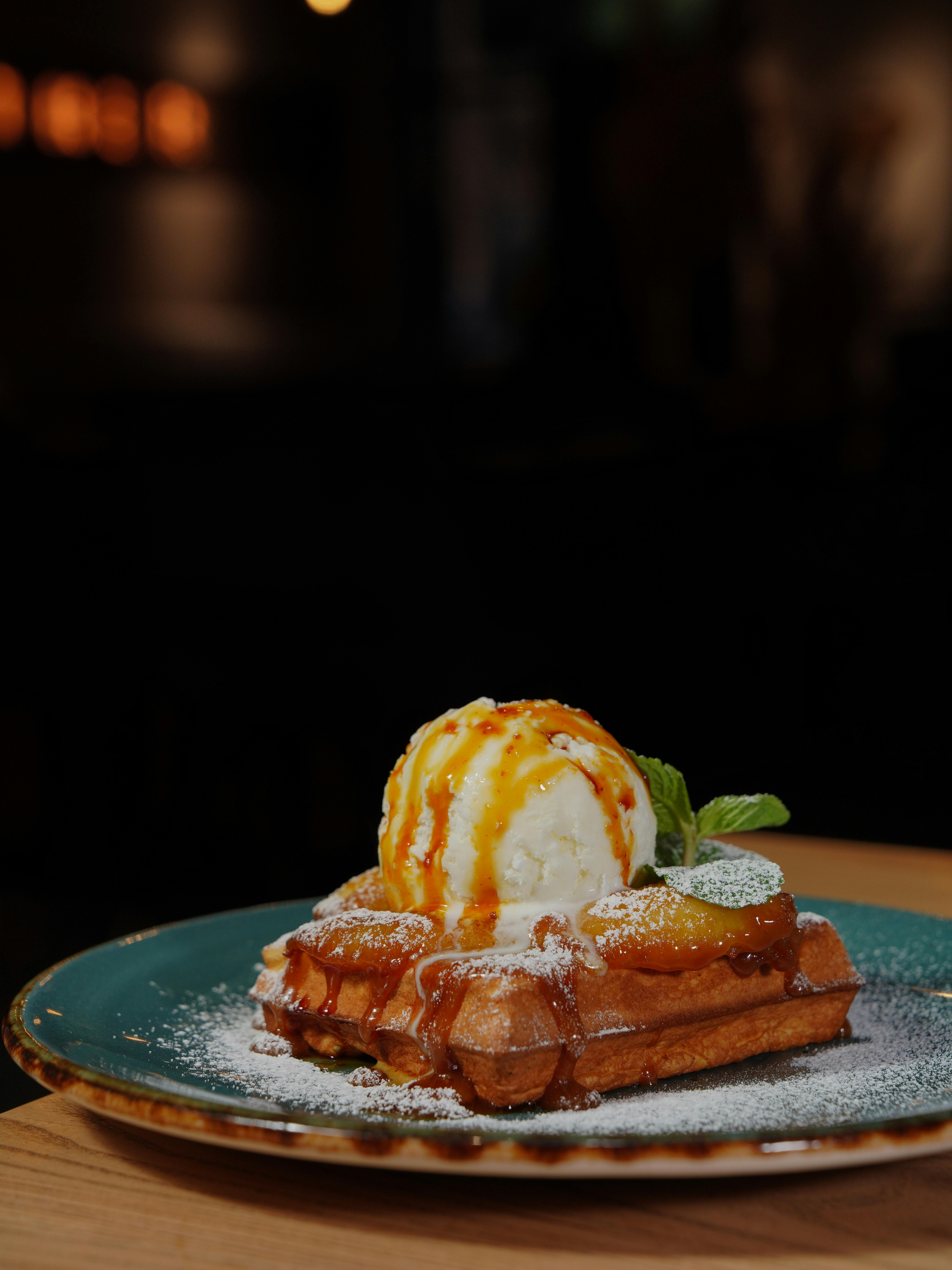 Appetizing waffles topped with ice cream and caramel sauce served on a stylish plate.