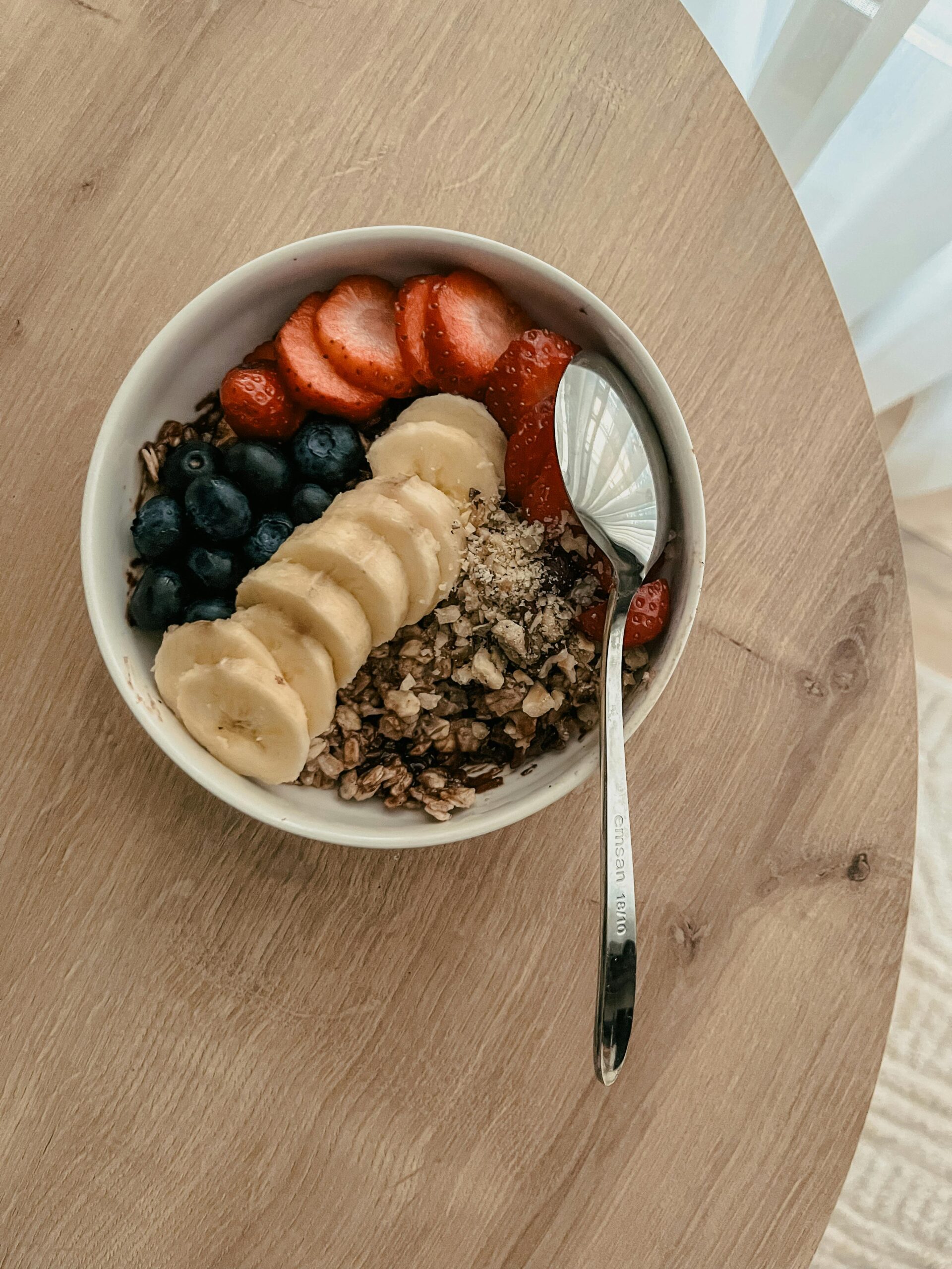 Nutritious bowl of granola with bananas, strawberries, and blueberries on a table.